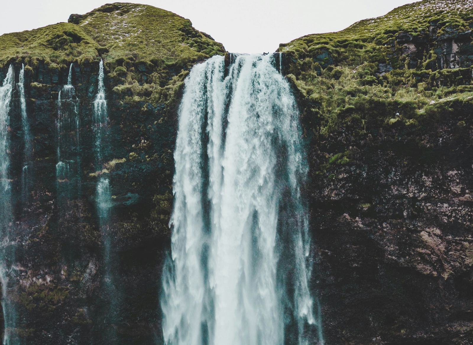 A vertical shot of a powerful, wide waterfall cascading down a cliff face, with a road or viewing area at its base.