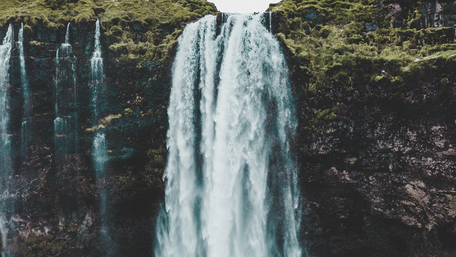 an image of a waterfall cascading during daytime with blue sky in the background