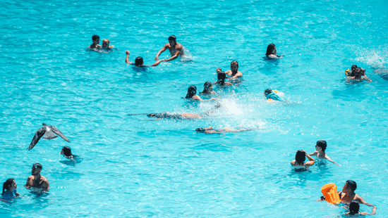 Aerial view of a large turquoise swimming pool filled with people enjoying a fun-filled swim on a sunny day.