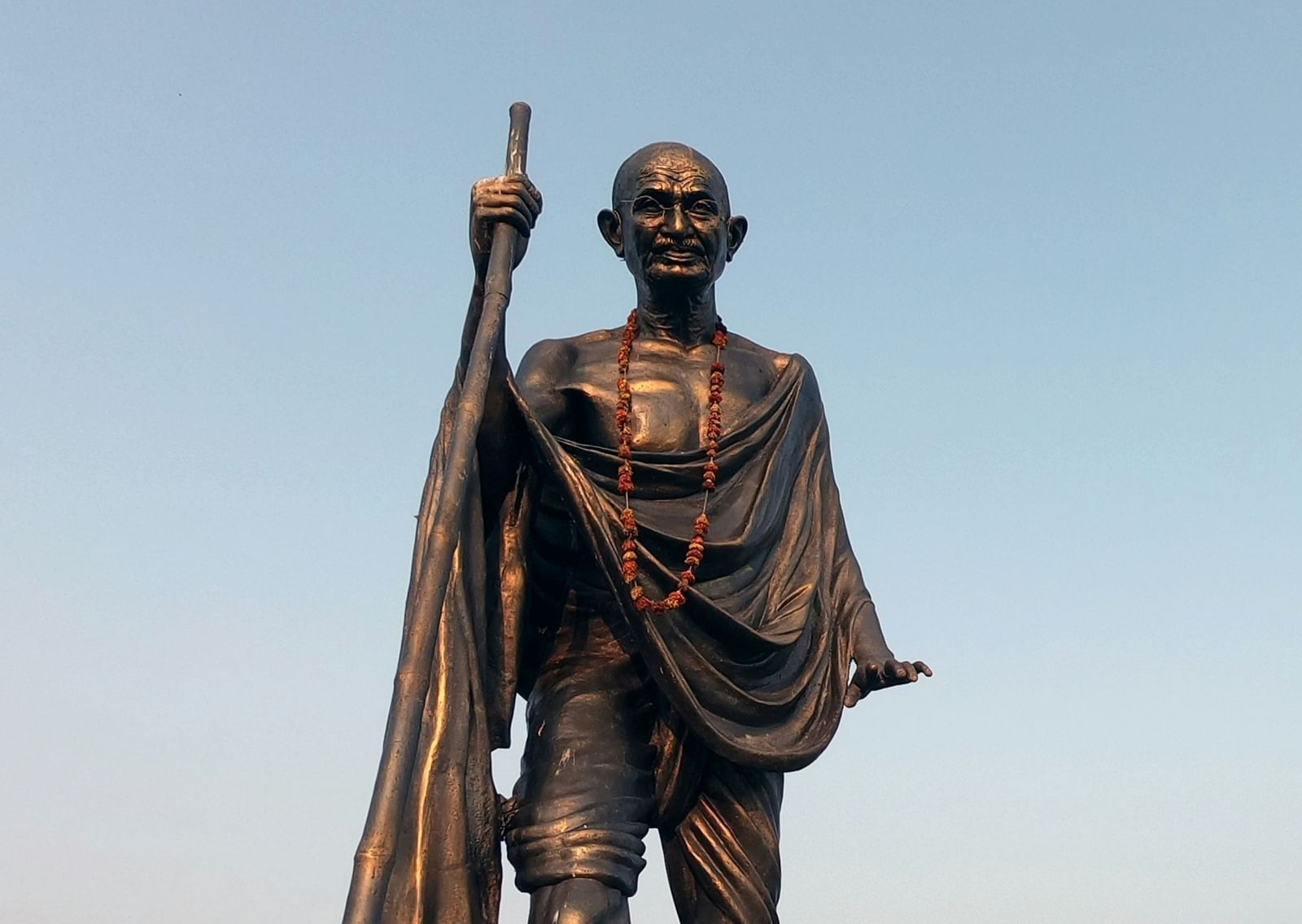 An overview of Mahathma Gandhi's statue holding a stick with blue sky in the background.