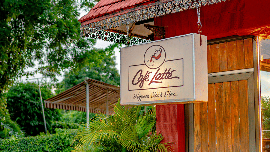 The exterior entrance signage of Café Latte at Noor-Us-Sabah Palace, Bhopal, hanging from a red-roofed structure surrounded by lush garden greenery.
