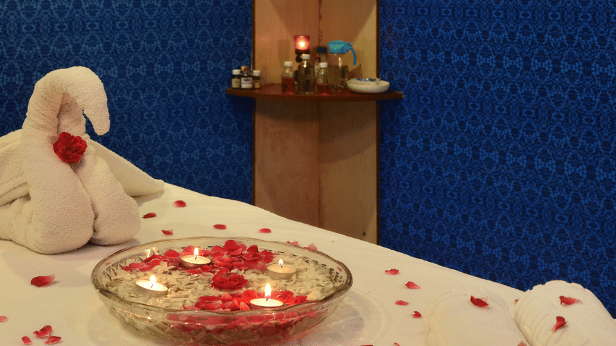 A spa bed with roses petals over it, a towel shaped like a duck and a wooden decor shelf with products