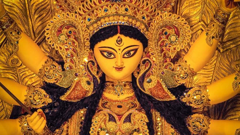 A vibrant idol of Goddess Durga adorned in traditional attire, with multiple arms holding symbolic items, set against a golden decorative backdrop.