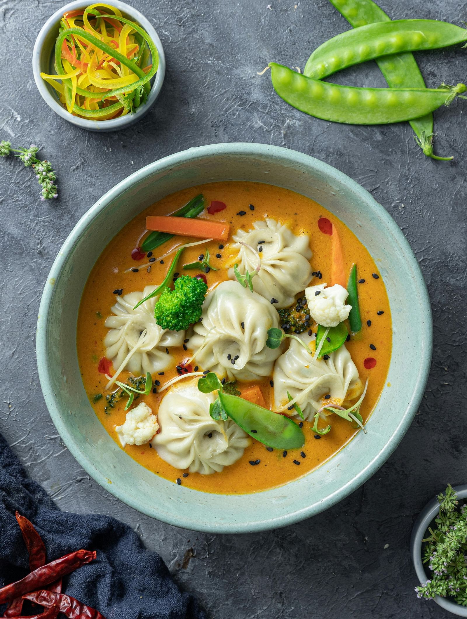 A top shot of a cyan coloured bowl with a piping hot serving of soupy dumplings served with thinly sliced salad.