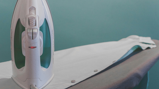 A close-up view of an iron resting upright on the fabric covered surface of an ironing board.