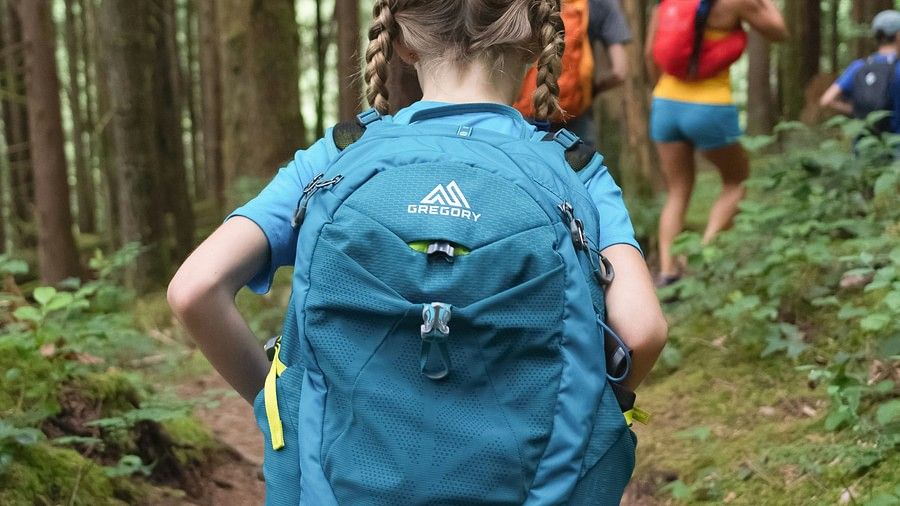 A girl carrying a backpack while trekking through the forest.