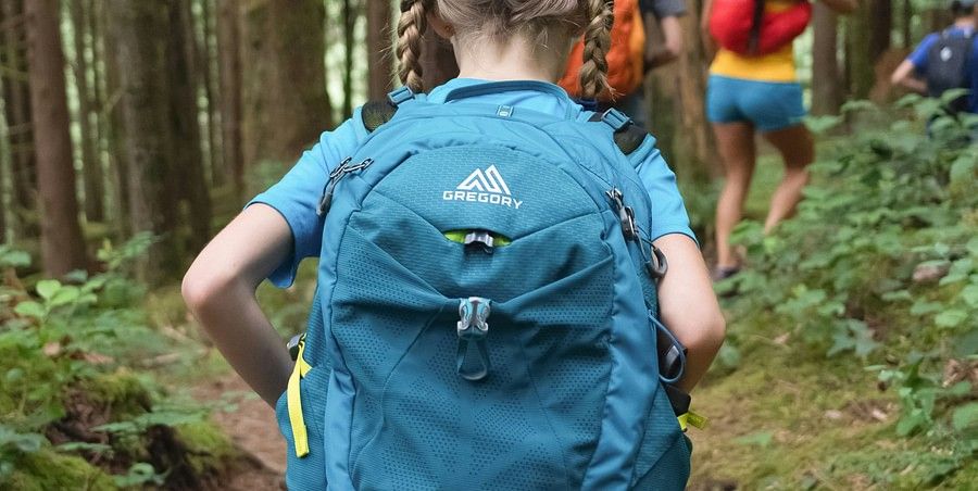 A girl carrying a backpack while trekking through the forest.