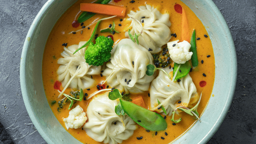 A top shot of a cyan coloured bowl with a piping hot serving of soupy sumplings served with thinly sliced salad.