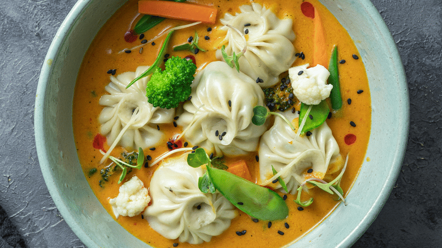 A top shot of a cyan coloured bowl with a piping hot serving of soupy sumplings served with thinly sliced salad.