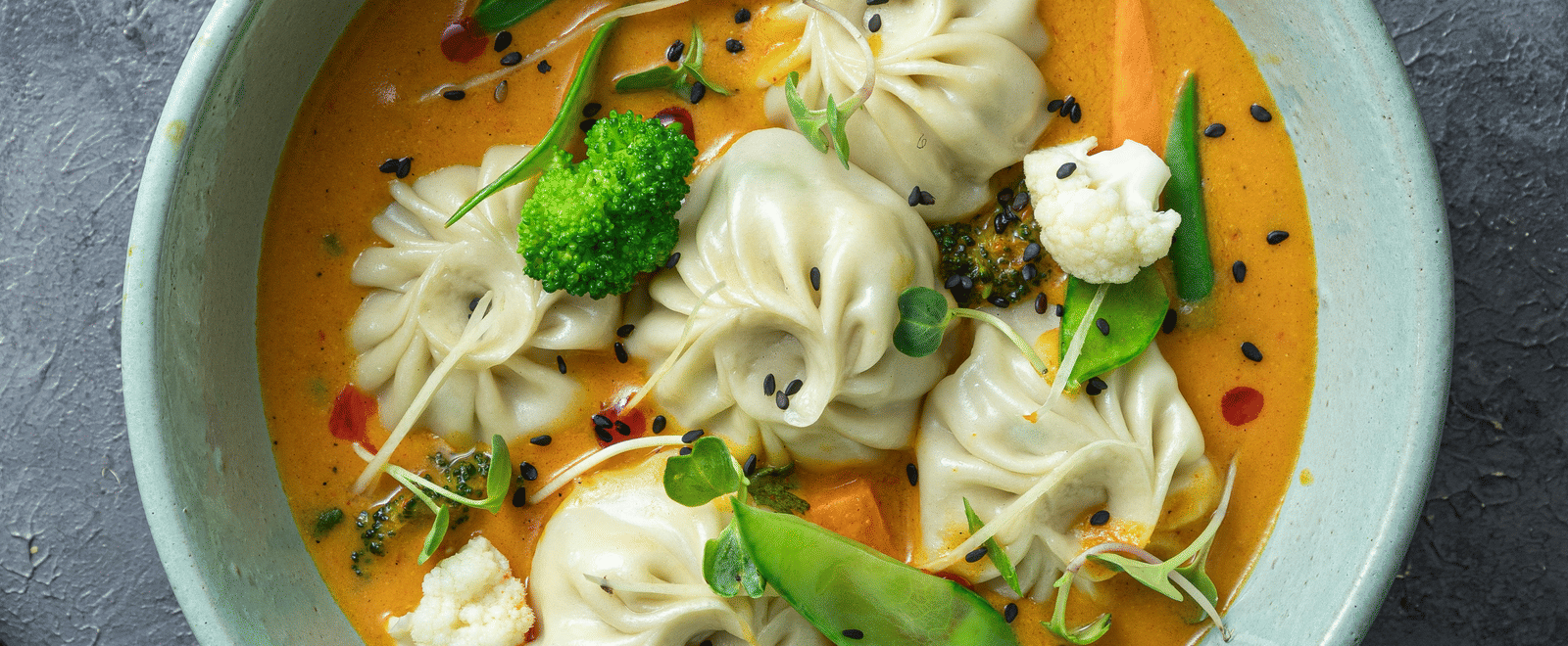 A top shot of a cyan coloured bowl with a piping hot serving of soupy dumplings served with thinly sliced salad.