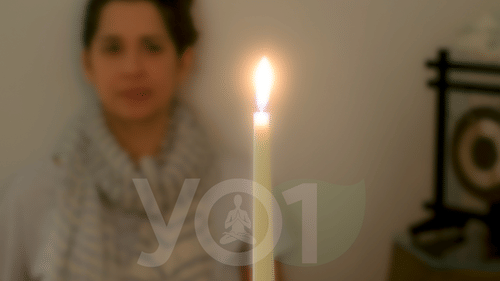 a person staring at a lit candle on a table in front of them in a semi-dark room at YO1 Longevity & Health Resorts
