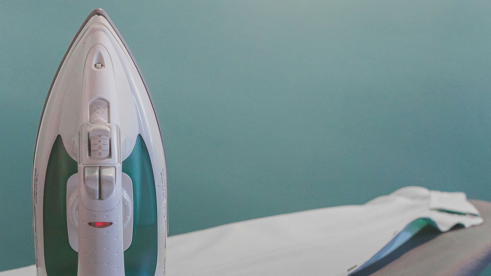 A white steam iron placed on an ironing board, with a light blue wall in the background.