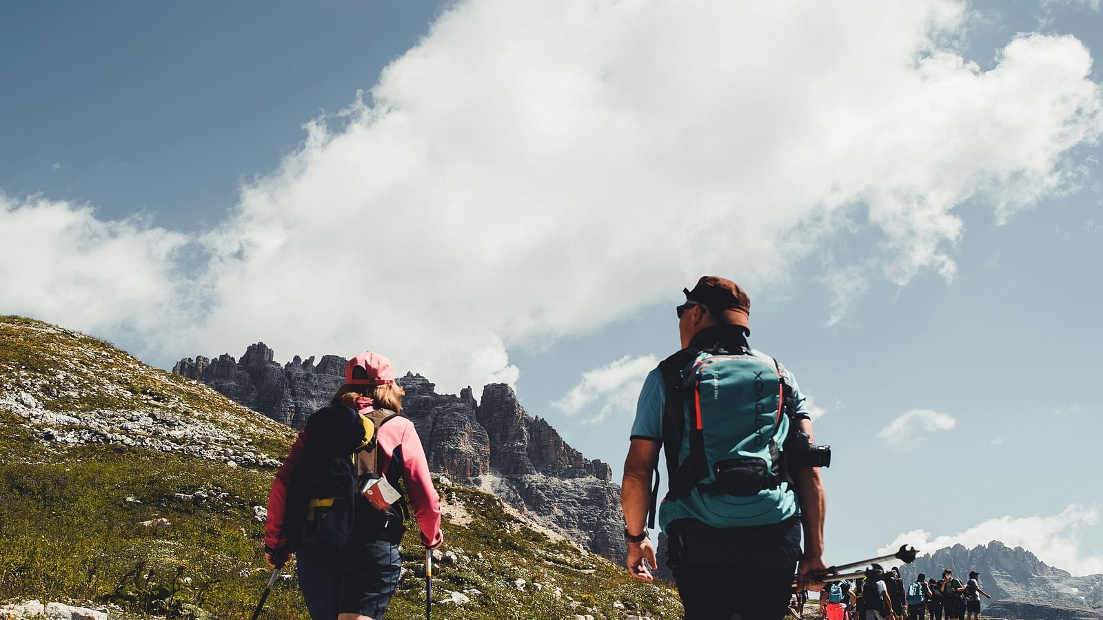 two people hiking on a dirt road with white clouds on blue sky in the background