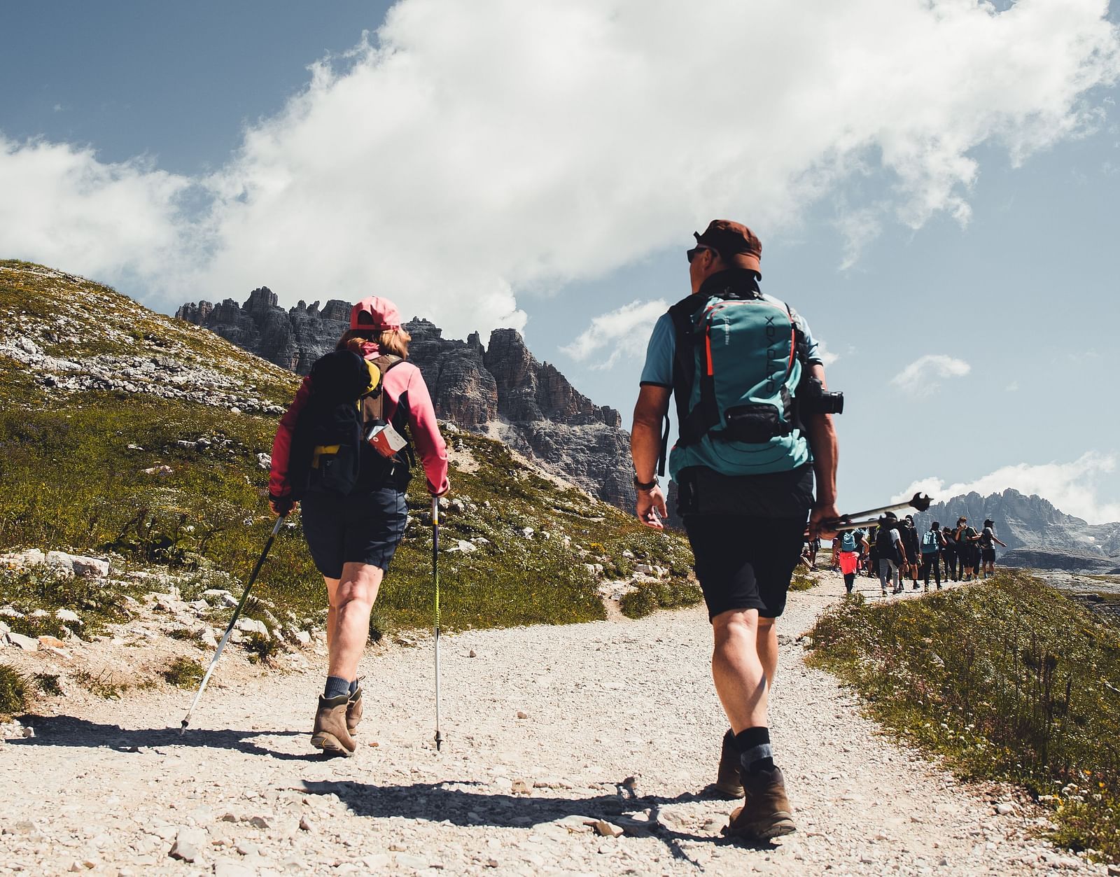 two people walking down a path during their trek with white clouds in the background