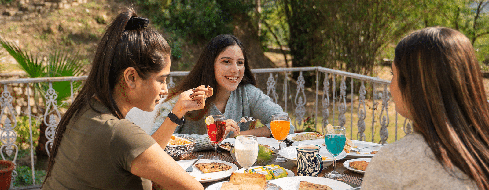 Three women enjoying food in an open setting of Bread and Brook at the Sylvan Retreat, Dehradun.