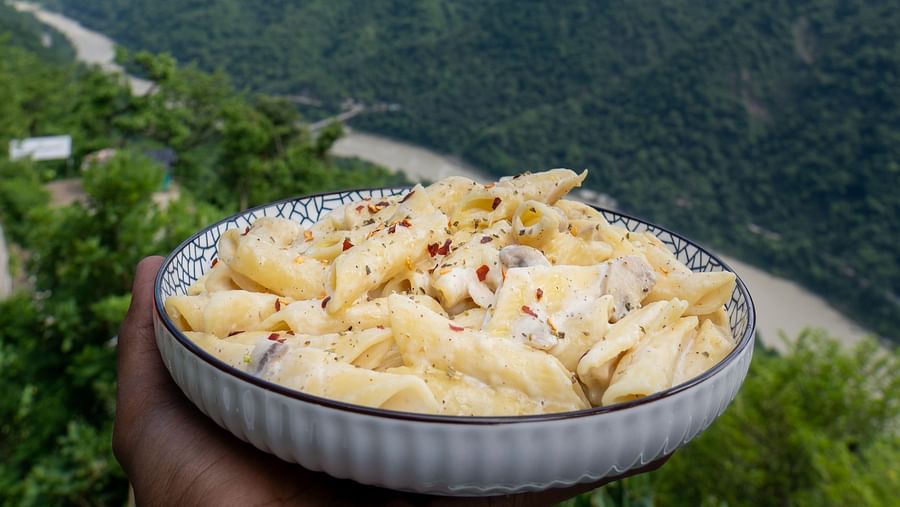 alfredo pasta served in a plate with a backdrop of mountains - Neer Ganga Resorts