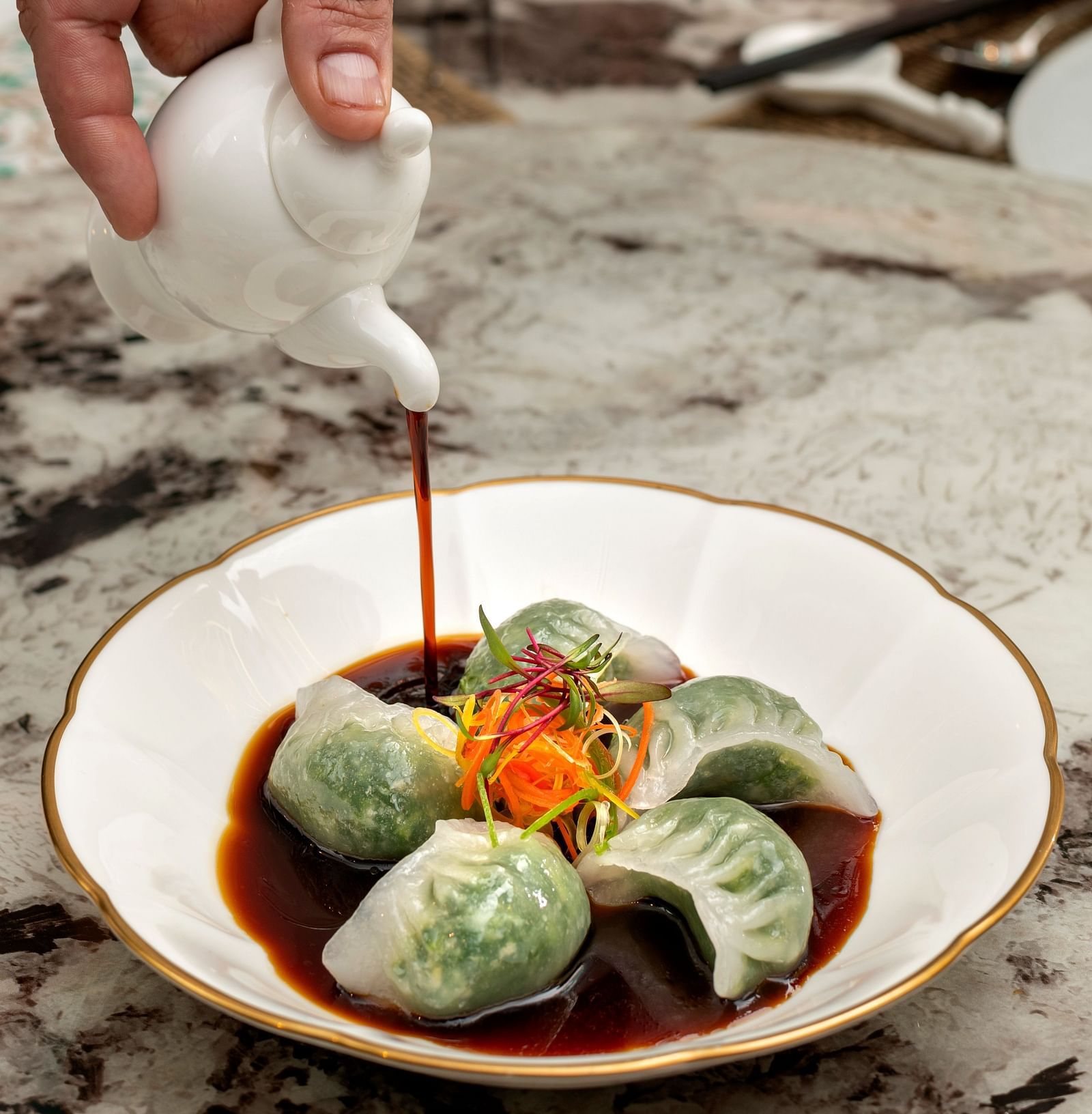 image of a plate of dim sums served with a dark coloured sauce poured over at the jade - The Claridges New Delhi