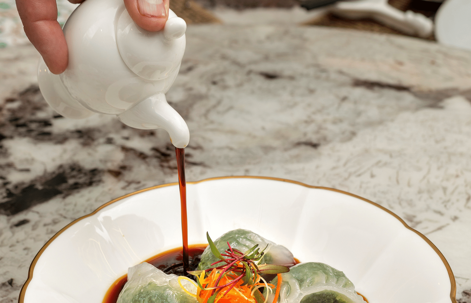 Image of a person pouring sauce on a pate of dumplings at The Claridges New Delhi