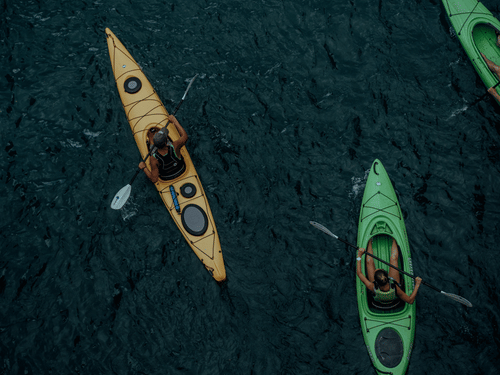 Two people kayaking across calm waters, paddling through a scenic setting during an outdoor water adventure.