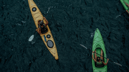 Two people kayaking across calm waters, paddling through a scenic setting during an outdoor water adventure.