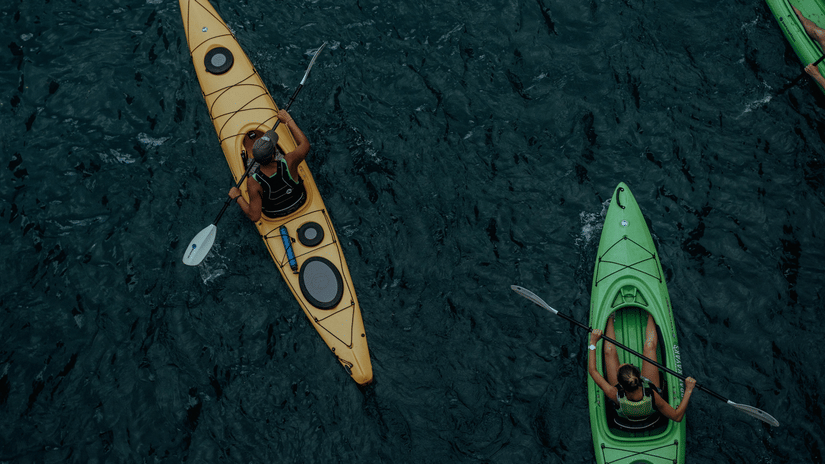 Two people kayaking across calm waters, paddling through a scenic setting during an outdoor water adventure.