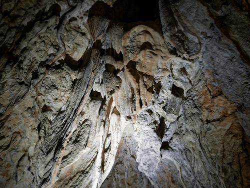 Illuminated limestone cave formations with dramatic stalactites and textured rock walls
