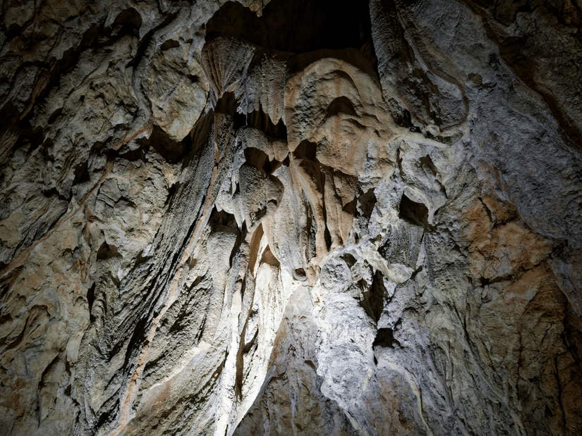 Illuminated limestone cave formations with dramatic stalactites and textured rock walls