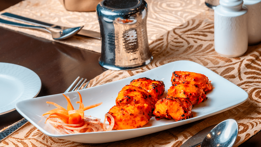 A plate of grilled tikkas served with a vegetable garnish on a formal table setting at Za-aiqa, Noor-Us-Sabah Palace, Bhopal.