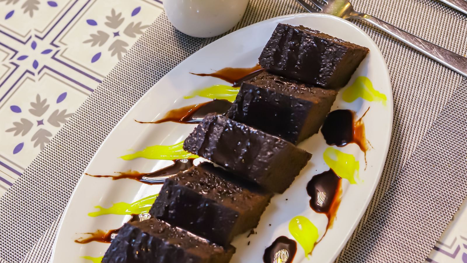An oval plate with dessert sits on a table with a floral arrangement at Vedikant Resorts The Mallard Corbett.