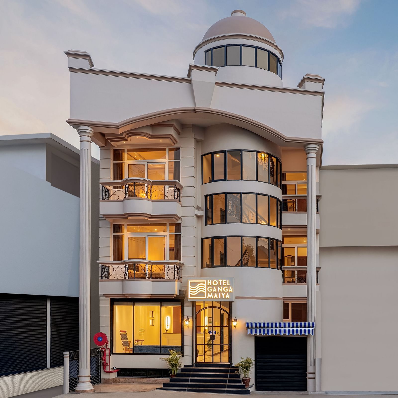Facade view of Hotel Ganga Maiya, with warm lighting radiating from inside, set against a cloudy sky | Hotel Ganga Maiya