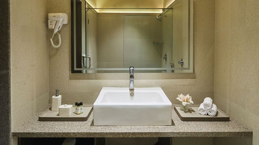 The bathroom vanity of Junior Suite with a rectangular sink, a large mirror, and neatly arranged white towels and toiletries at DGV Resort by Treat, Silvassa