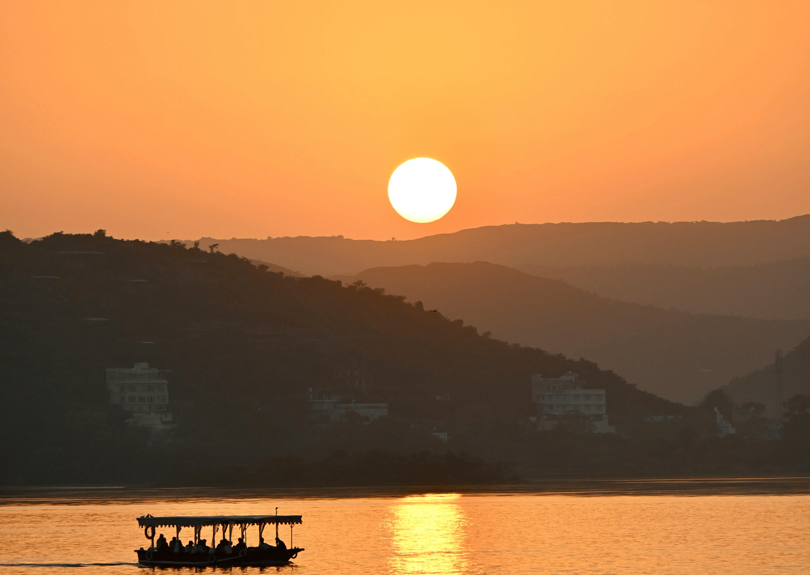 A yellow sunset over a lake, with the sun just touching the horizon line, casting a golden reflection on the water with a small boat silhouette.