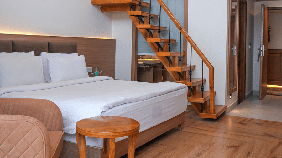 A loft suite with a queen size bed on the lower floor and wooden stairs leading up to an upper level at Ramada by Wyndham Mussoorie Mall Road.