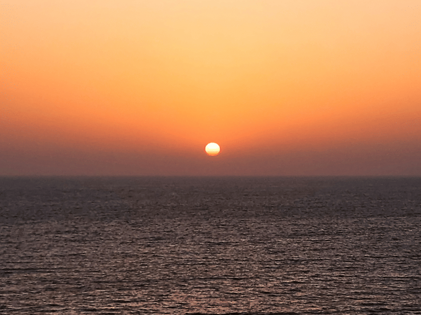 Golden sunset descending over the Arabian Sea with calm waves reflecting warm orange hues across the horizon at Juhu Beach.