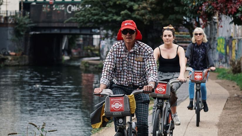 a group of people cycling next to a waterbody on a small path with greenery in the background