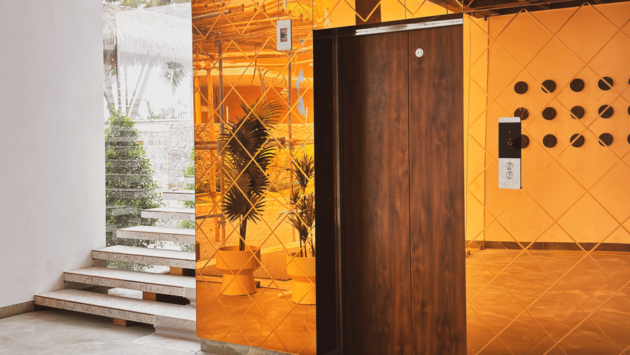 A wooden lift door is set into a wall of orange reflective tiles next to a short flight of white stairs at Avanya Resorts N Retreat.