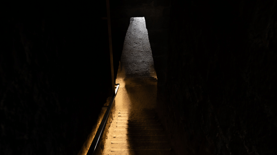 An overview of an entrance to a cave with light shining down only on one part of the steps at Sita Gufa.