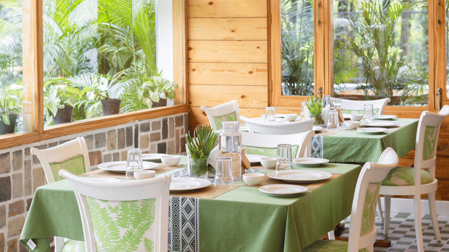 A cosy indoor dining space with green chairs, white tables, and large windows - Megha Resort & Villas, Dehradun