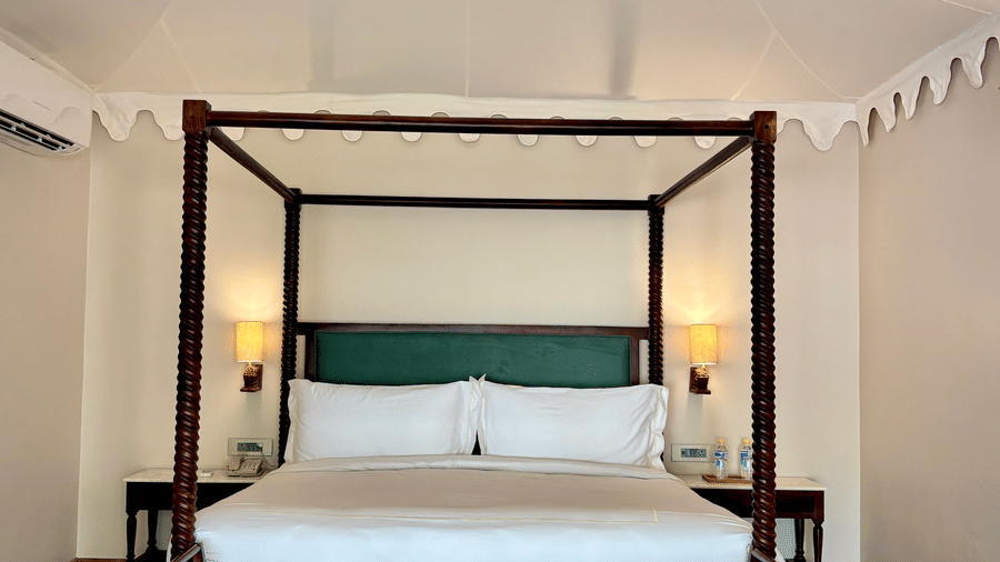 King size bed at Vana Suite featuring poster bed, bedside table with lamp, and a sofa  attached to the bed at Surpura Bagh