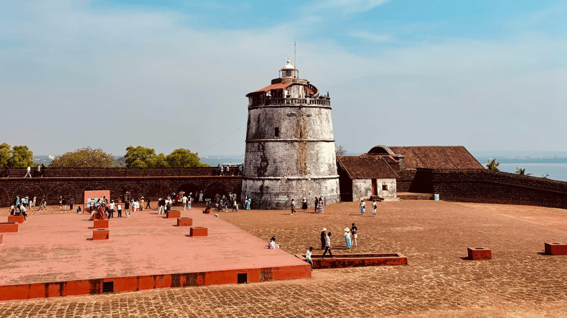 An ancient stone tower standing in a dry, open courtyard with terracotta-coloured platforms under a bright blue sky.