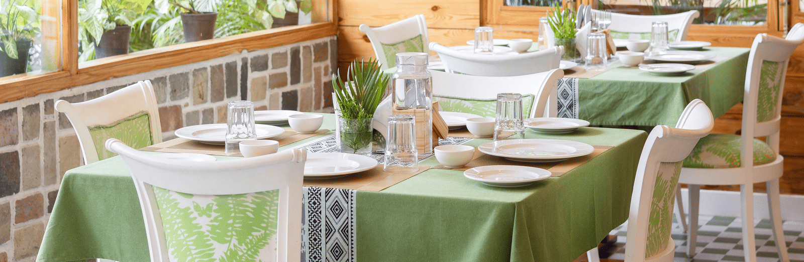 A cosy indoor dining space with green chairs, white tables, and large windows - Megha Resort & Villas, Dehradun