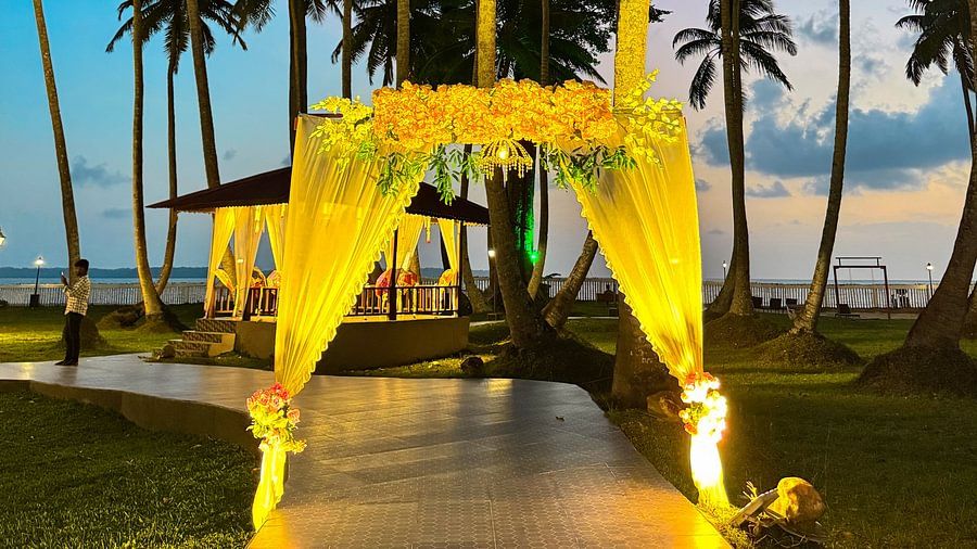 An outdoor pathway with a floral arch and palm trees at Silver Sand Sea Princess Beach Resort, Port Blair, leading to the beach.
