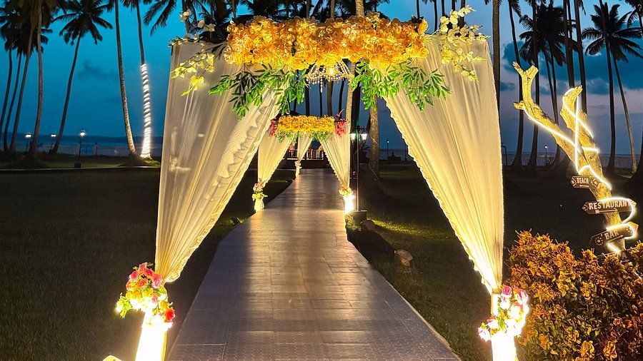Palm trees line an outdoor pathway with floral arches at Silver Sand Sea Princess Beach Resort, Port Blair, seen at dusk.