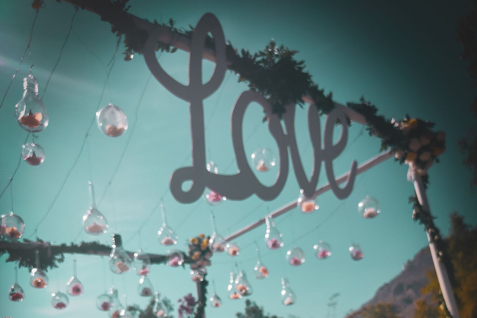 A whimsical outdoor setting with a LOVE sign, hanging glass ornaments, and floral arrangements.