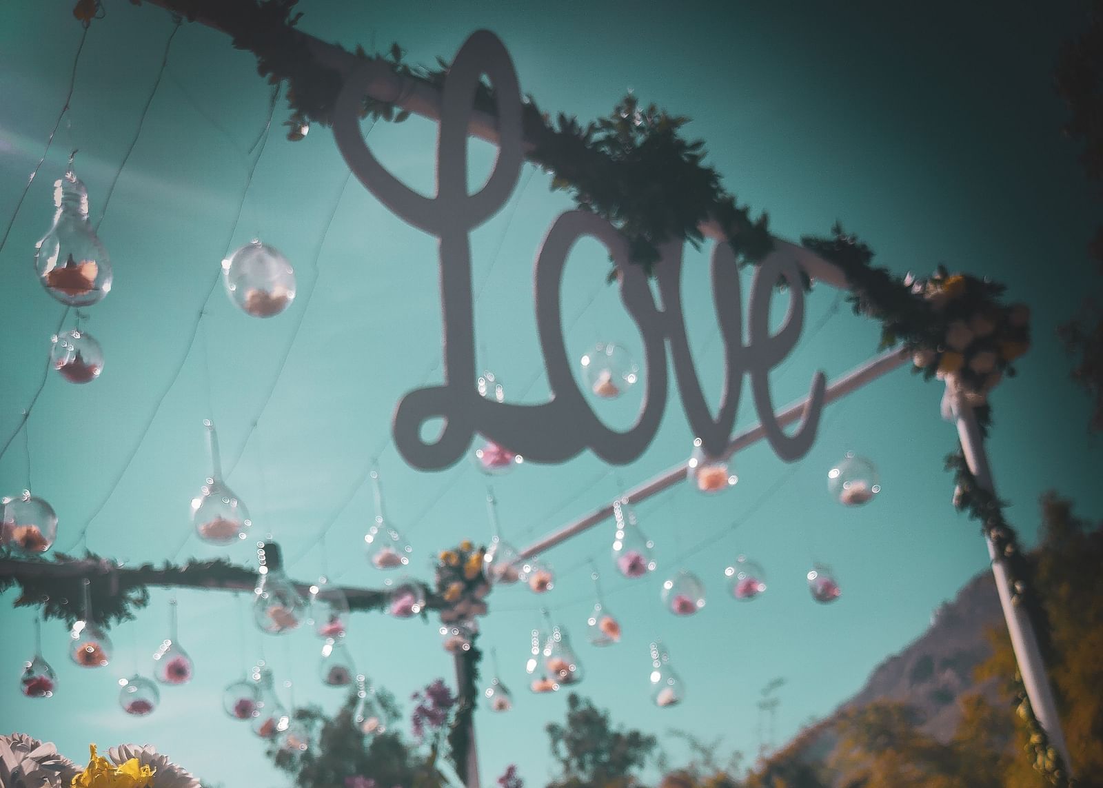 A whimsical outdoor setting with a LOVE sign, hanging glass ornaments, and floral arrangements.