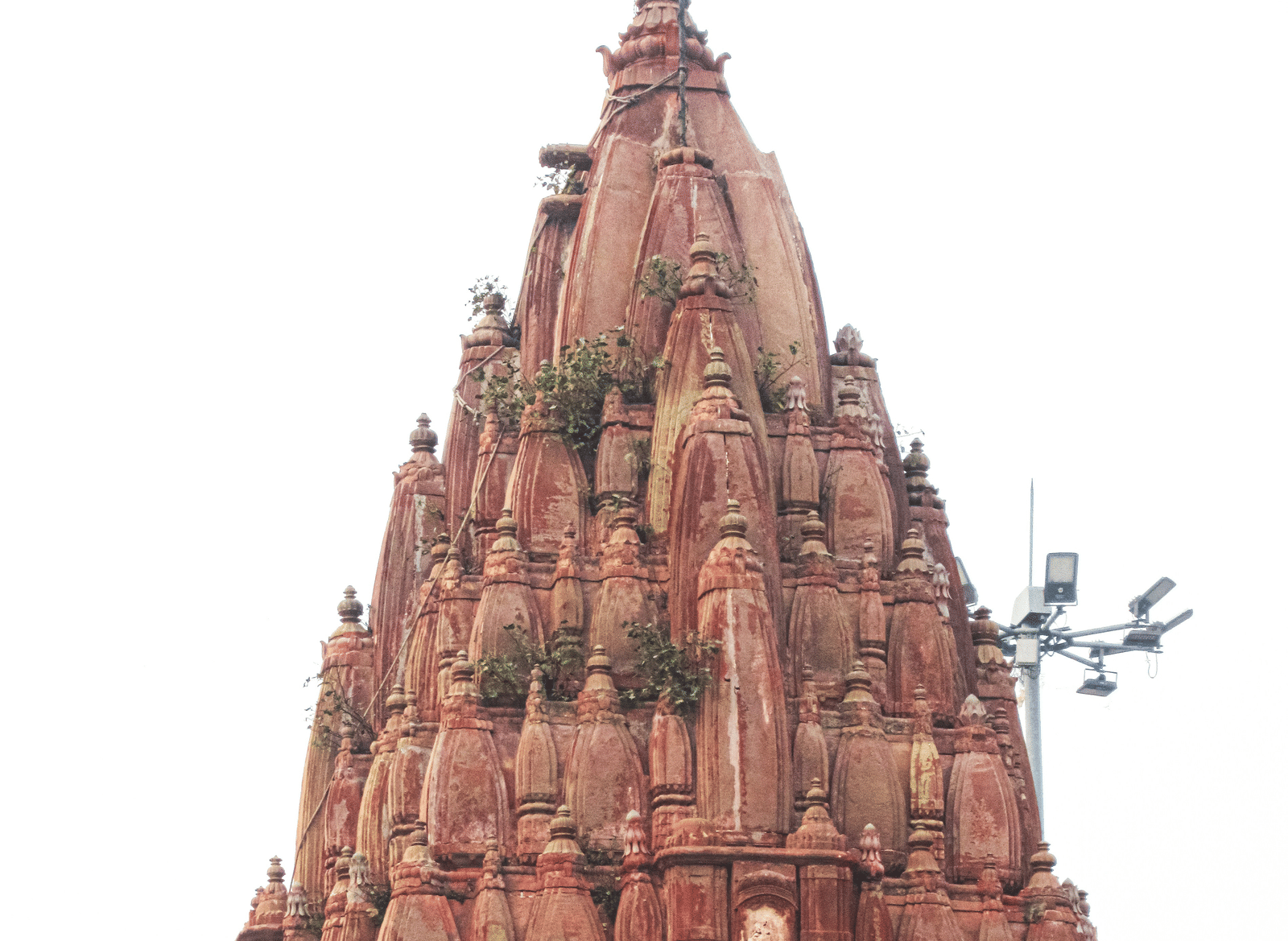 A tall, reddish-brown spire of a centuries-old temple stands starkly against a white sky.