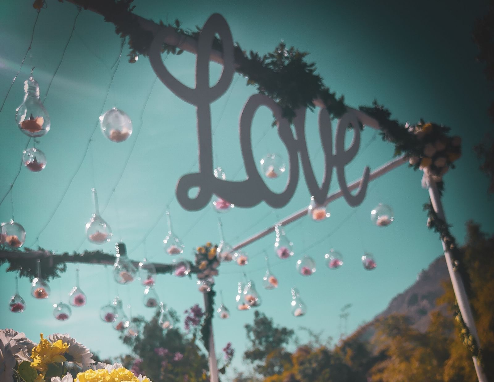 A whimsical outdoor setting with a LOVE sign, hanging glass ornaments, and floral arrangements.