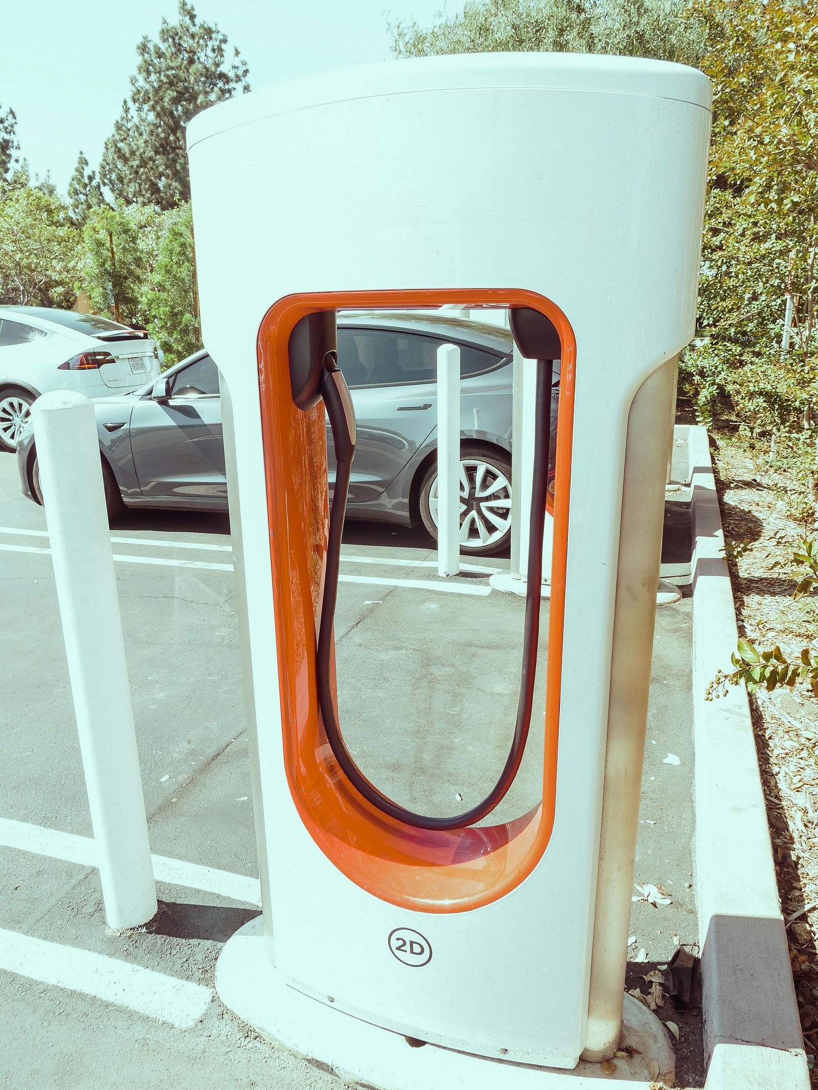 A modern electric vehicle charging station stands outdoors in a car park.