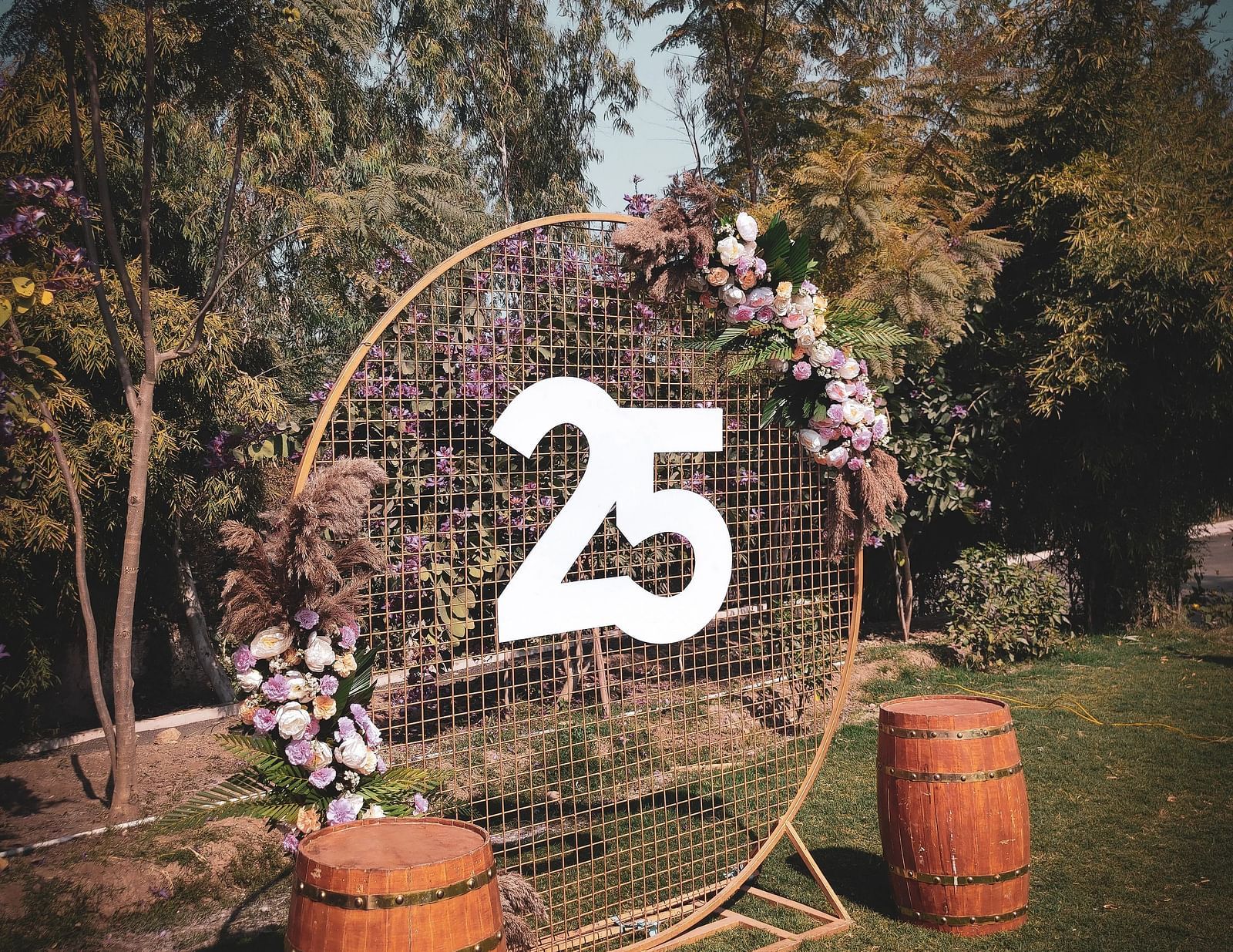An outdoor decor with '25' sign surrounded with barrels, lights, and trees.