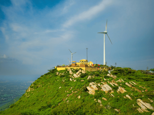 A far view of the Chitradurga windmills overlooking lush green fields with a bright blue sky in the background
